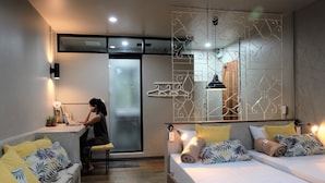 Una habitación de hotel moderna con sofá, cama con almohadones estampados tropicales, escritorio con computadora portátil y un panel decorativo en la pared.