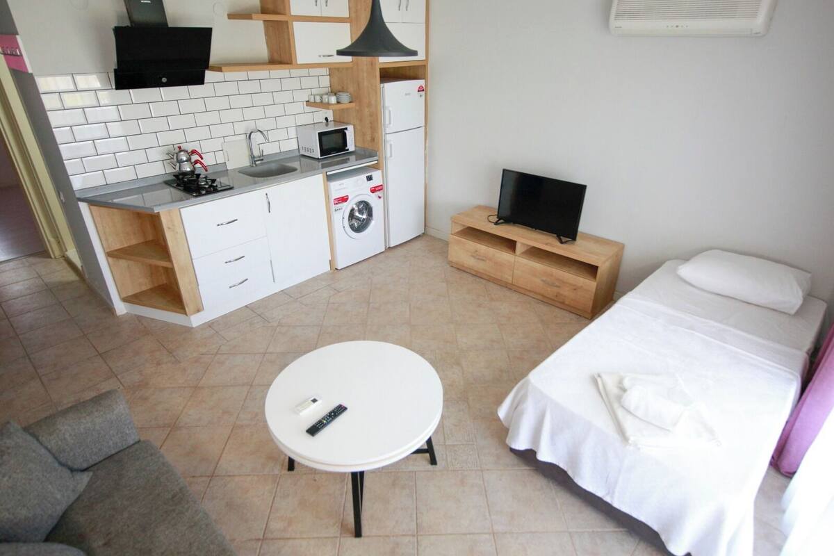 A compact hotel room with a kitchenette, a single bed, a small table, and a TV.