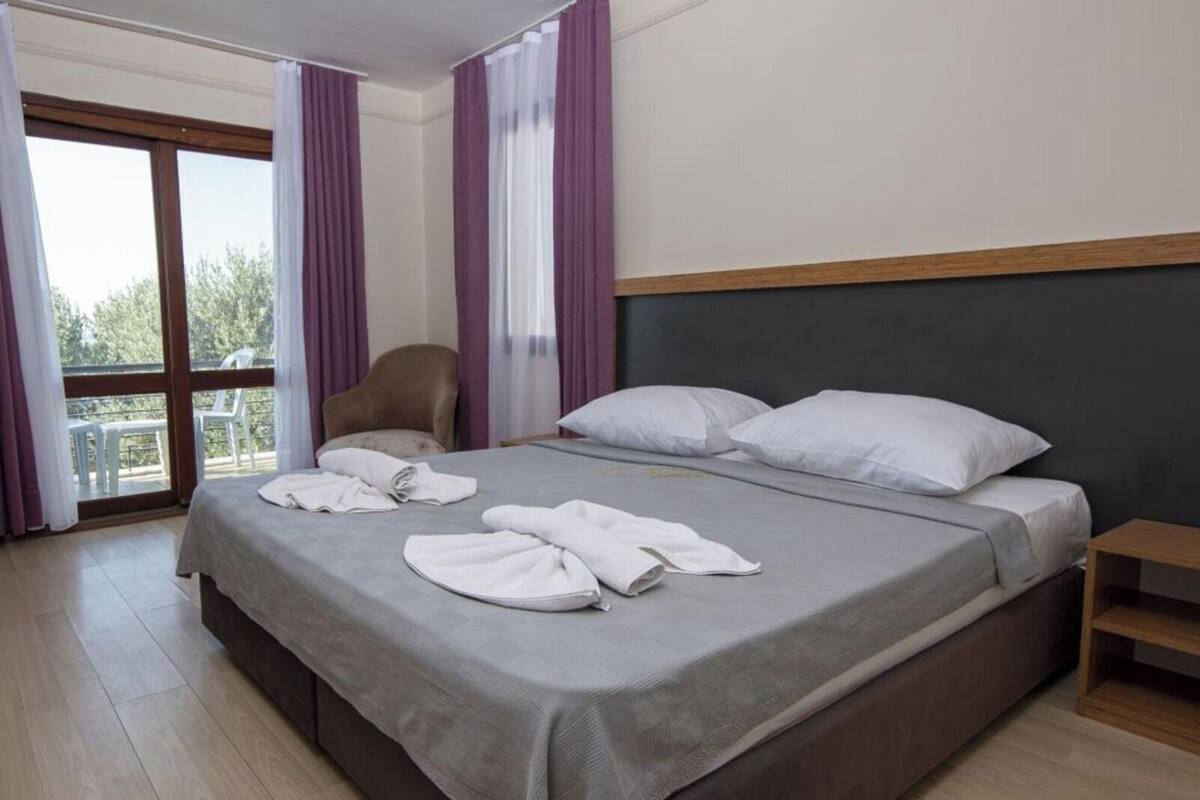 A hotel room with a large bed, a chair, and a balcony view.