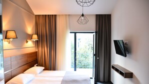 Een hotelkamer met een groot bed, twee bedlampen, een aan de muur bevestigde televisie en een glazen schuifdeur naar een balkon.