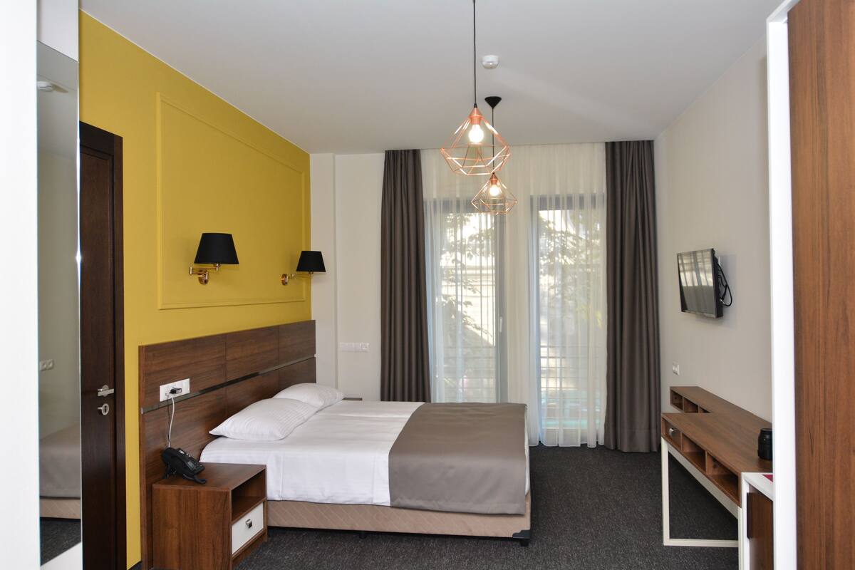 A hotel room with a bed, bedside tables, a desk, and a TV.