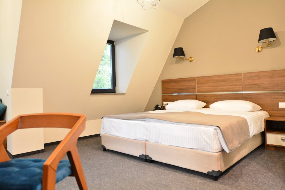 A bedroom with a bed, a chair, a nightstand, a lamp, and a window.