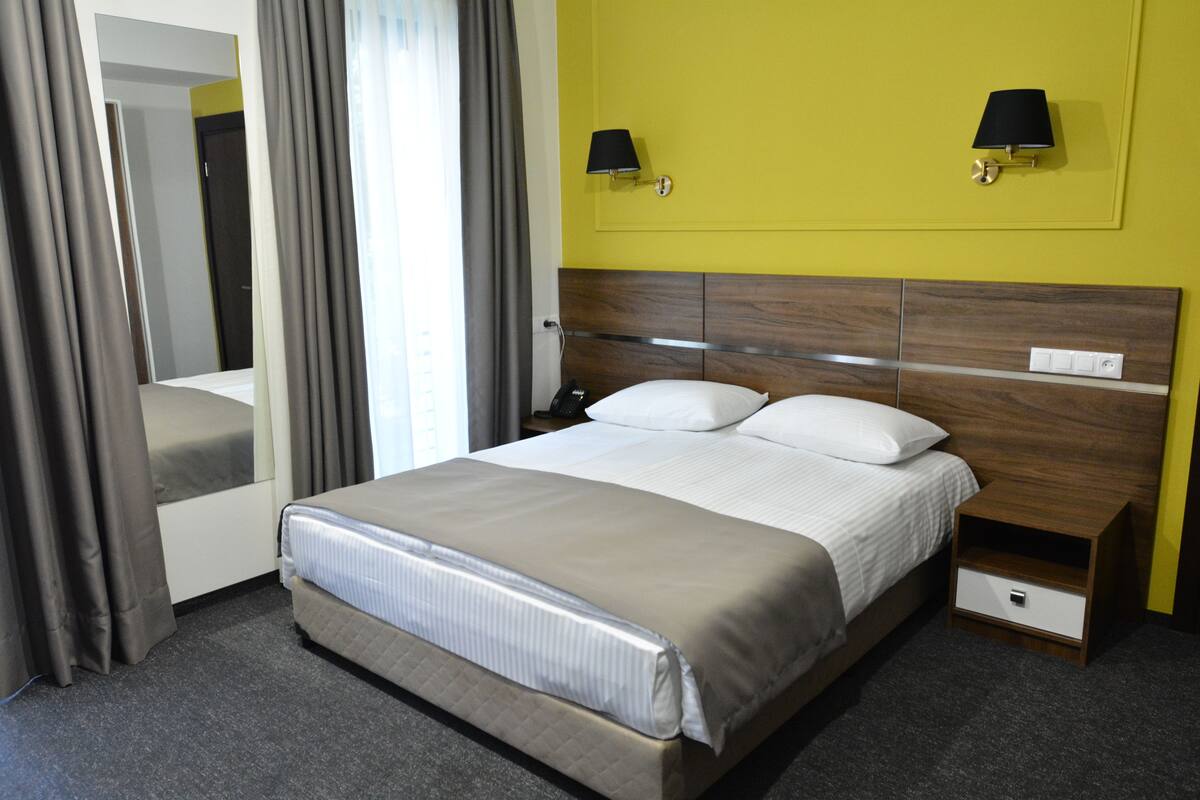 A hotel room with a large bed, bedside tables, a nightstand, a mirror, and two wall-mounted lamps.
