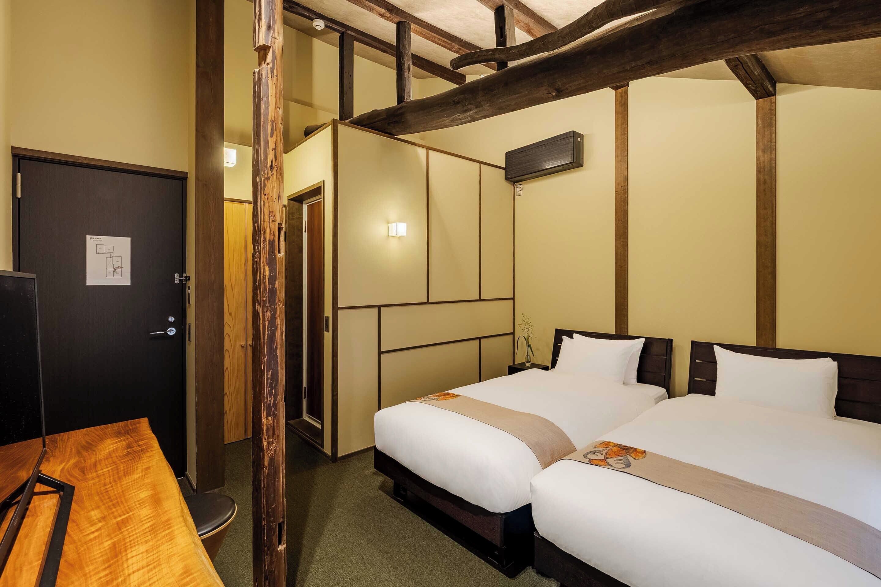 A hotel room with two beds, a wooden table, and a door with a sign.