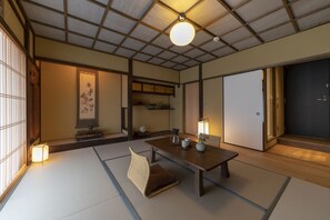 A traditional Japanese room with tatami flooring, a low wooden table, a cushioned chair, and sliding doors. - THE MACHIYA Kamiumeya (Kyoto)
