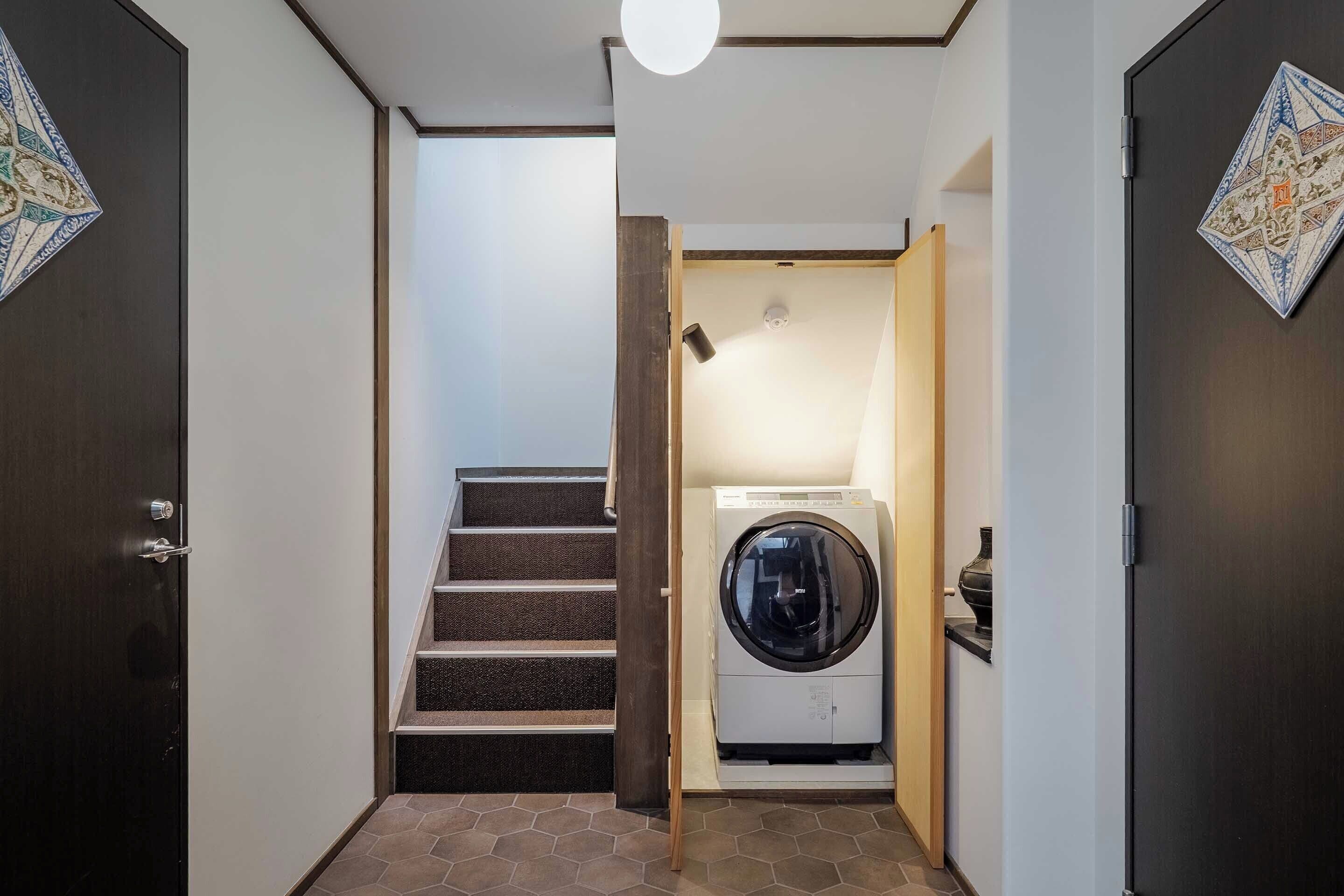 A laundry room with a washing machine, a staircase, and a door with a decorative tile.