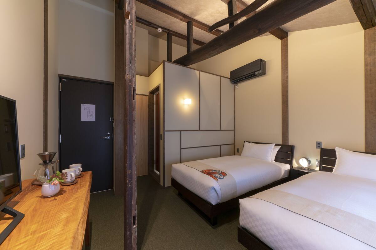 Une chambre d’hôtel avec deux lits, un bureau en bois avec une machine à café et un miroir.