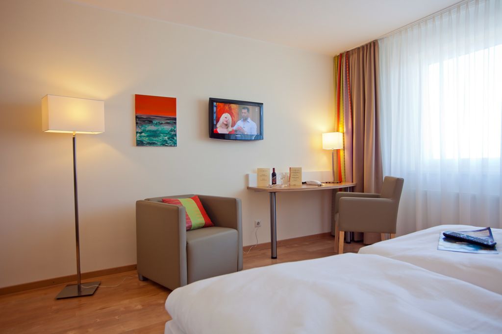 Ein Hotelzimmer mit zwei Betten, einem Schreibtisch mit Stuhl, einer Couch, einem Fernseher und einer Lampe.