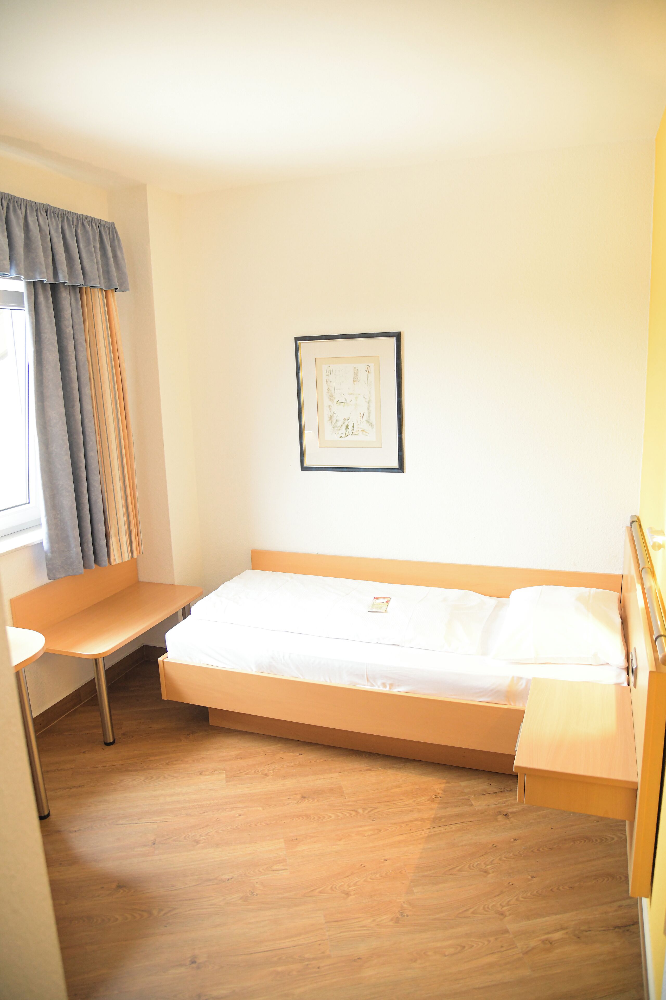 A compact hotel room with a single bed, a small desk, and a window with curtains.
