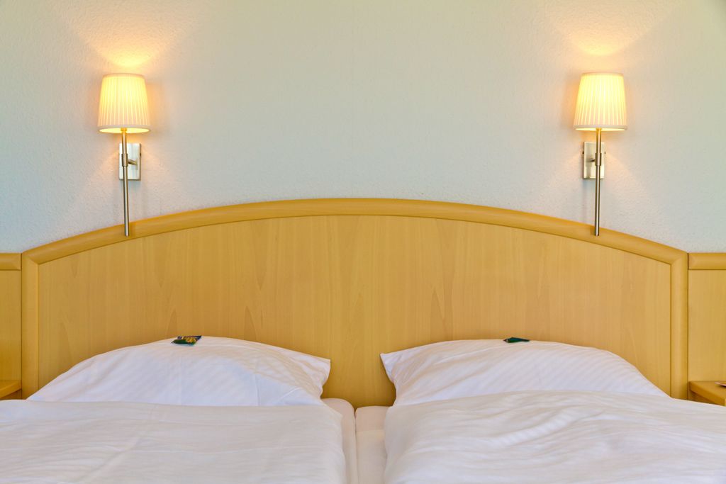 A double bed with a wooden headboard, two bedside lamps, and a white wall.
