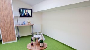 Una habitación con alfombra verde, una mesa redonda con botellas, un televisor en la pared y un panel de madera.
