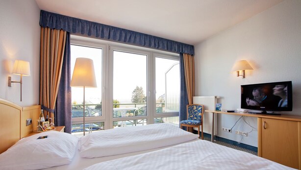 Una habitación de hotel con dos camas, televisión, una silla y ventana con cortinas.