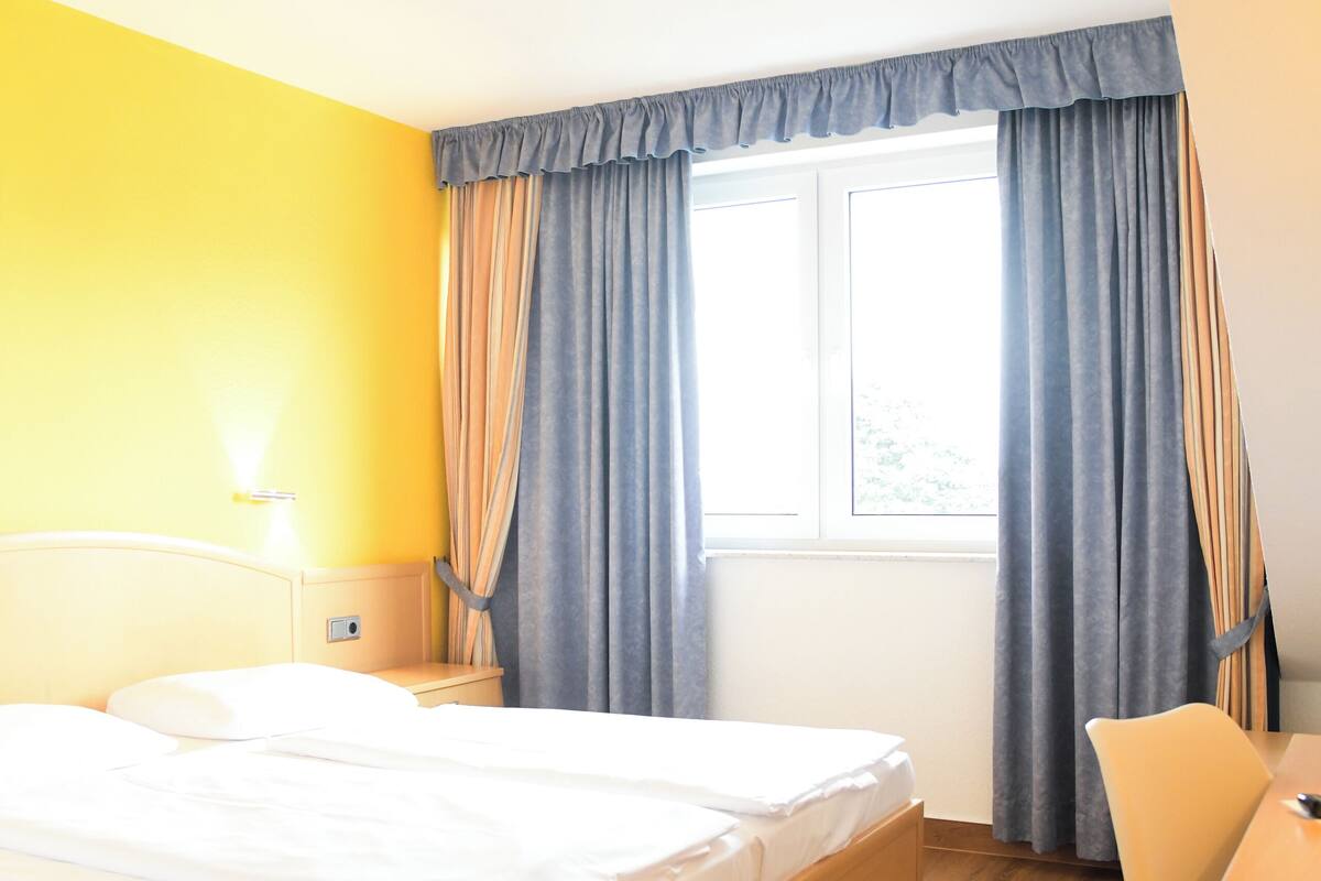 A hotel room with a wooden bed, a desk, and a window with curtains.