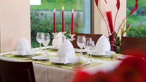 Una mesa de comedor dispuesta con servilletas blancas, copas de vino y velas rojas.