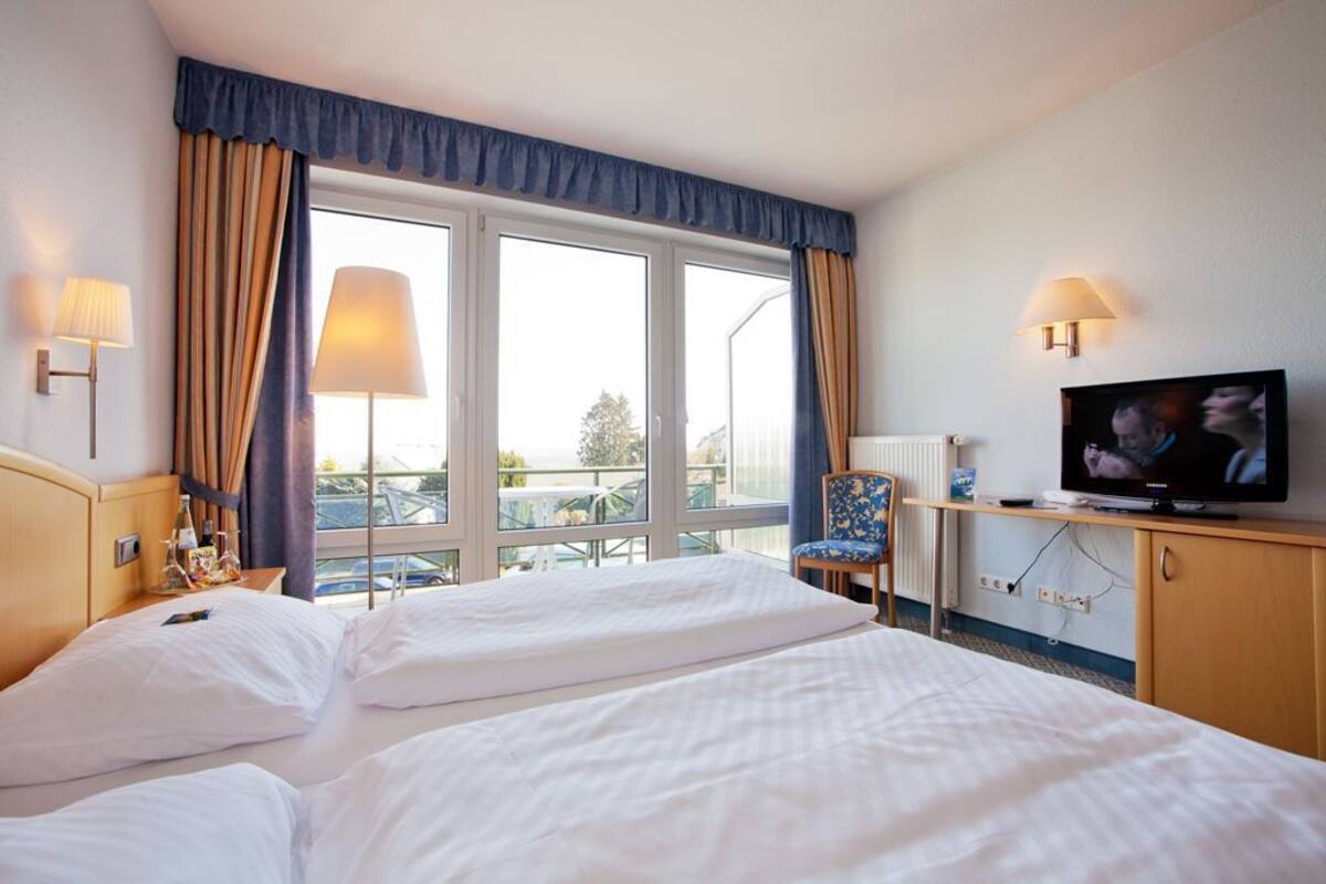 A hotel room with two beds, a television, a chair, and a view of the outdoors.