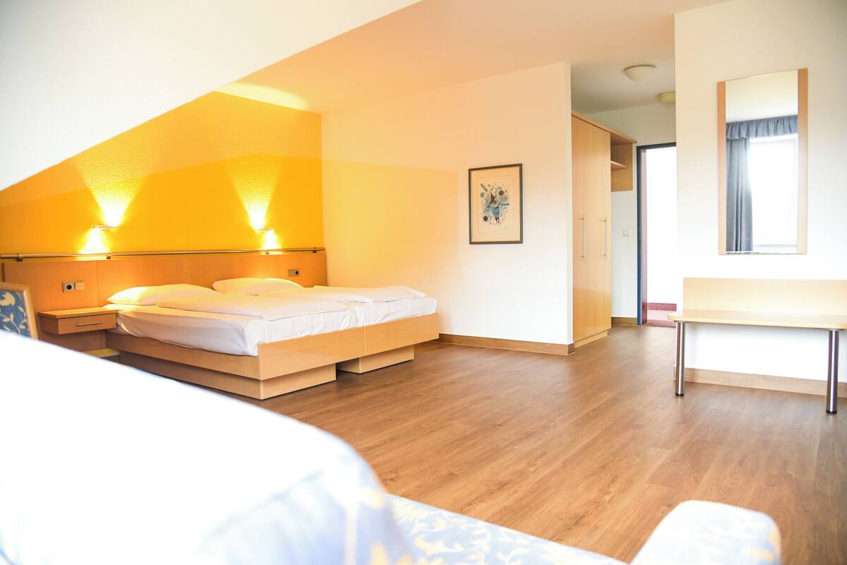 A bedroom with a bed, bedside lamps, a desk, and a window.