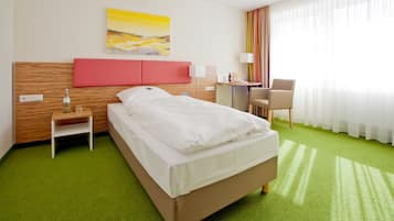 A hotel room with a bed, a desk, a chair, a nightstand, and a painting on the wall.
