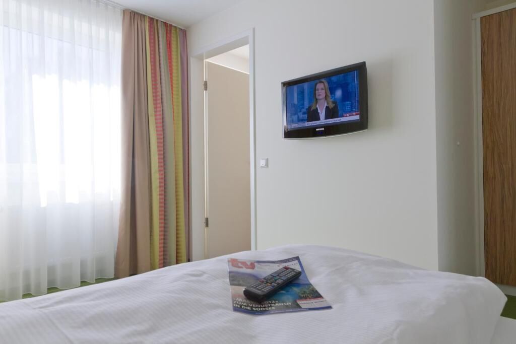 A hotel room with a bed, a TV mounted on the wall, and a magazine on the bed.