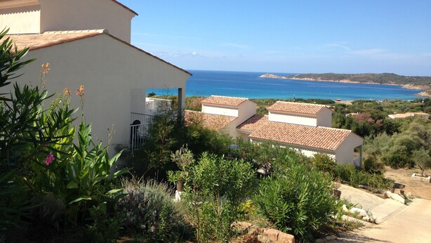 A coastal villa with a view of the sea, surrounded by greenery and a clear sky. - Résidence Castugna (Cargese)