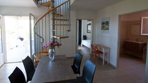 A dining area with a table, chairs, a vase with flowers, a staircase, and a view of the outside. - Résidence Castugna (Cargese)