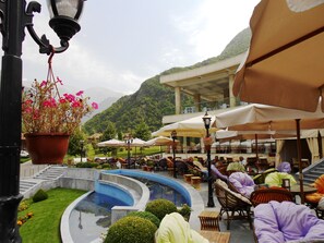 An outdoor seating area with umbrellas, a pool, and a mountainous backdrop. - Sheki Park (Sheki)