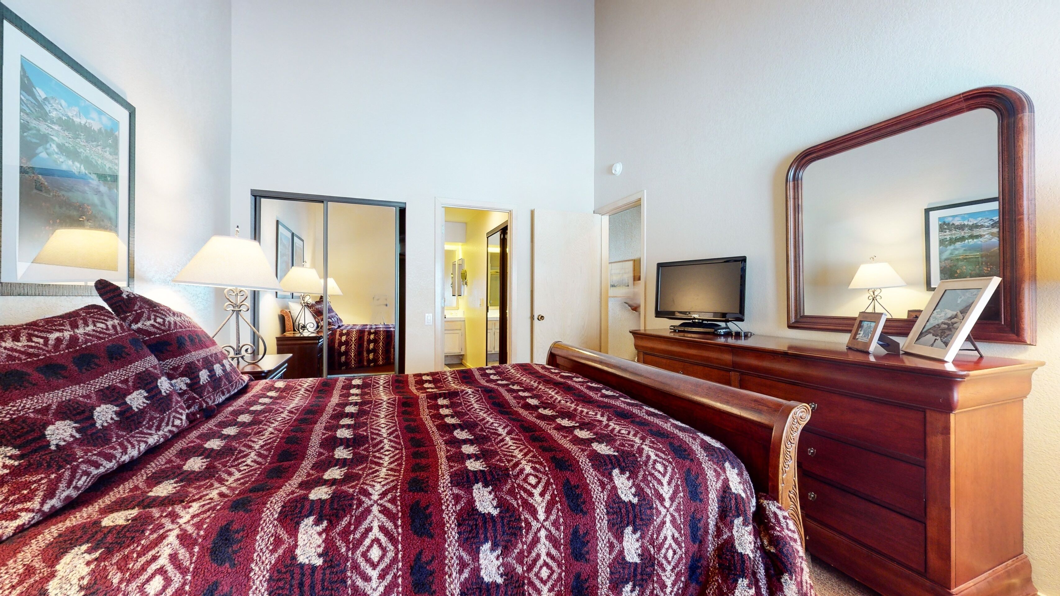 A hotel room with a large bed, a wooden dresser, a television, and a mirror.