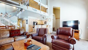 Relax in this stylish living area with a sofa, armchair, and coffee table, featuring a flat-screen TV and kitchenette.