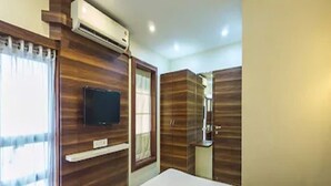Habitación de hotel con una cama, un televisor montado en la pared, una ventana con cortinas y paneles de madera en las paredes.