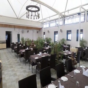 A spacious indoor dining area with multiple tables and chairs, large windows, and ceiling fans.