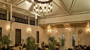 Un comedor espacioso con varias mesas y sillas, una lámpara central y luces decorativas.