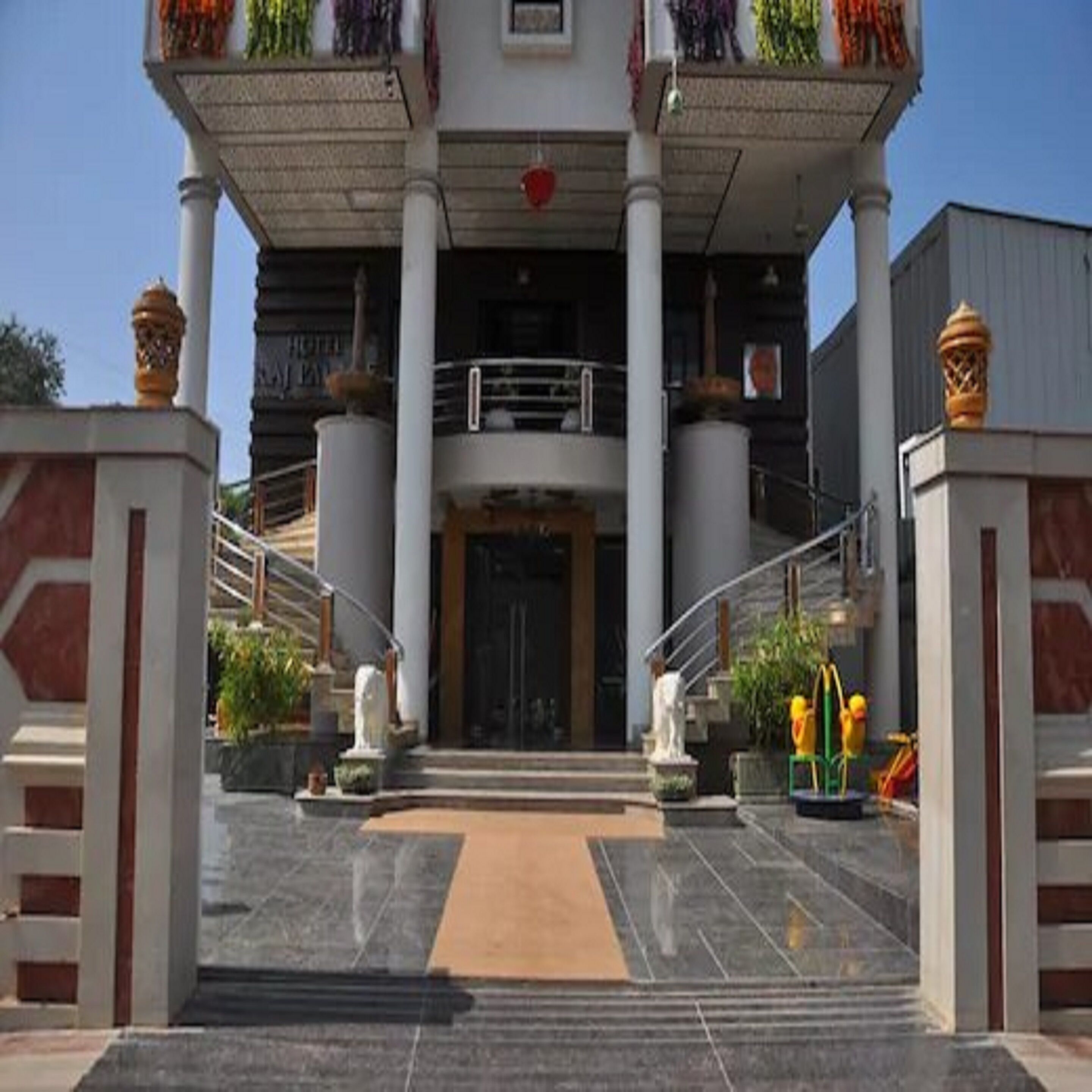 A hotel entrance with a central staircase, a covered balcony, and a large door.