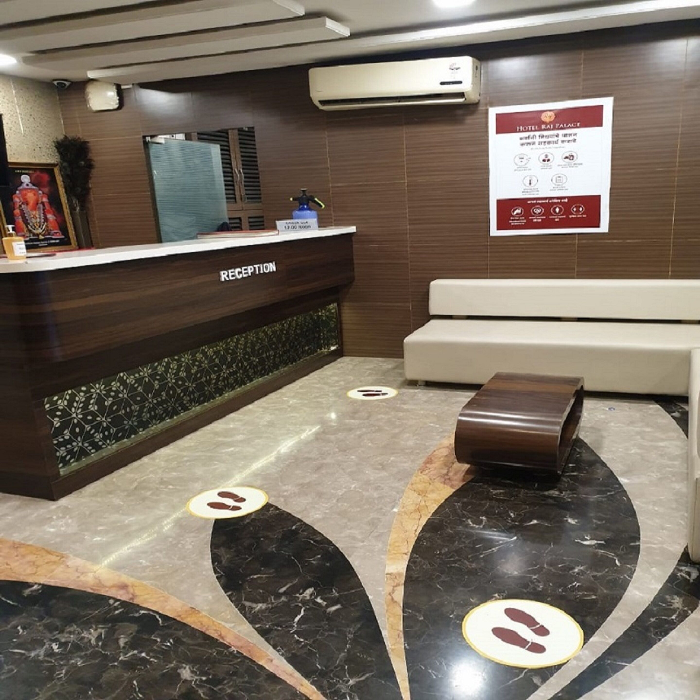 A hotel reception area with a reception desk labeled "RECEPTION," a waiting area with a sofa, and a poster on the wall with hotel information.