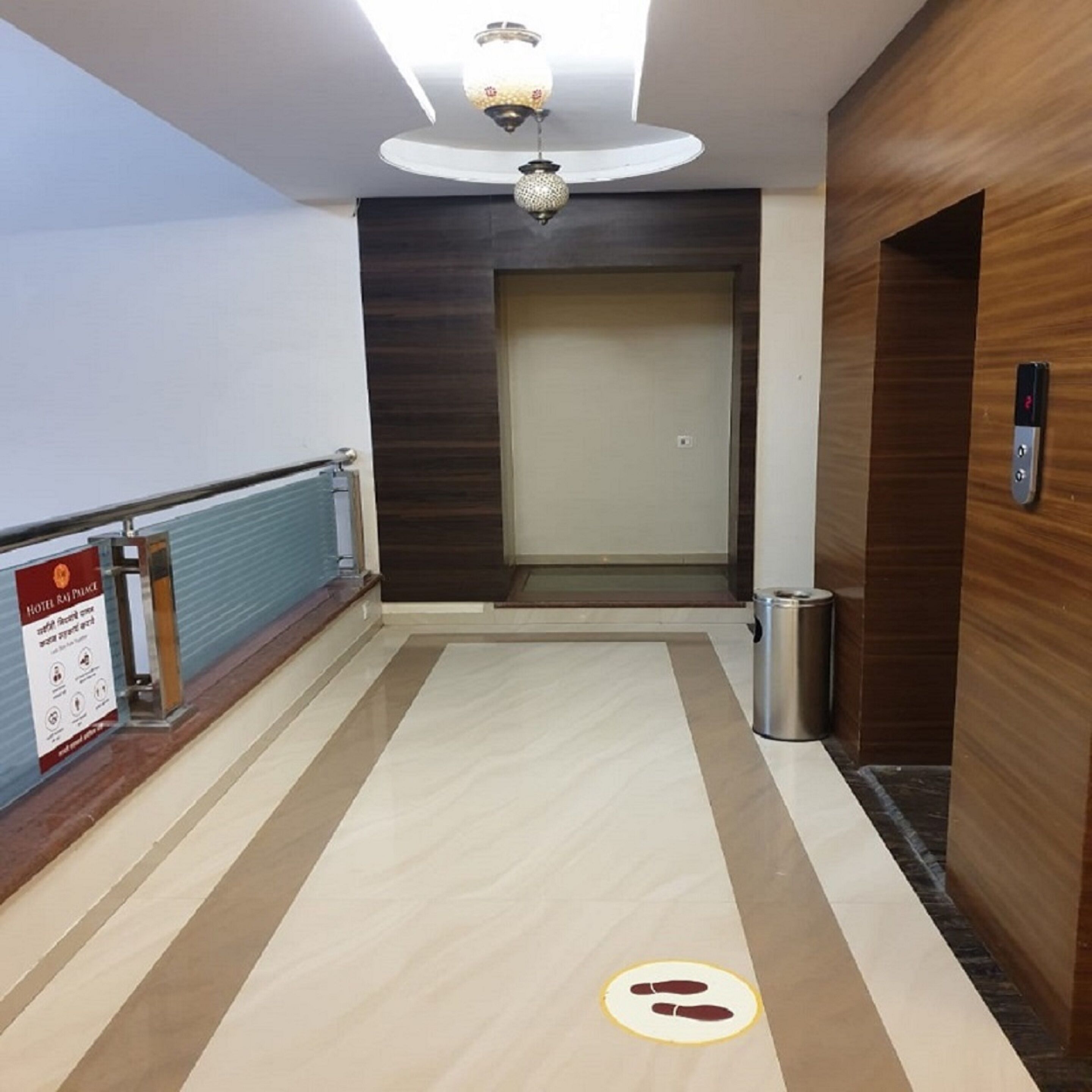 A hotel corridor with a wooden wall, a trash bin, and a sign on the left.