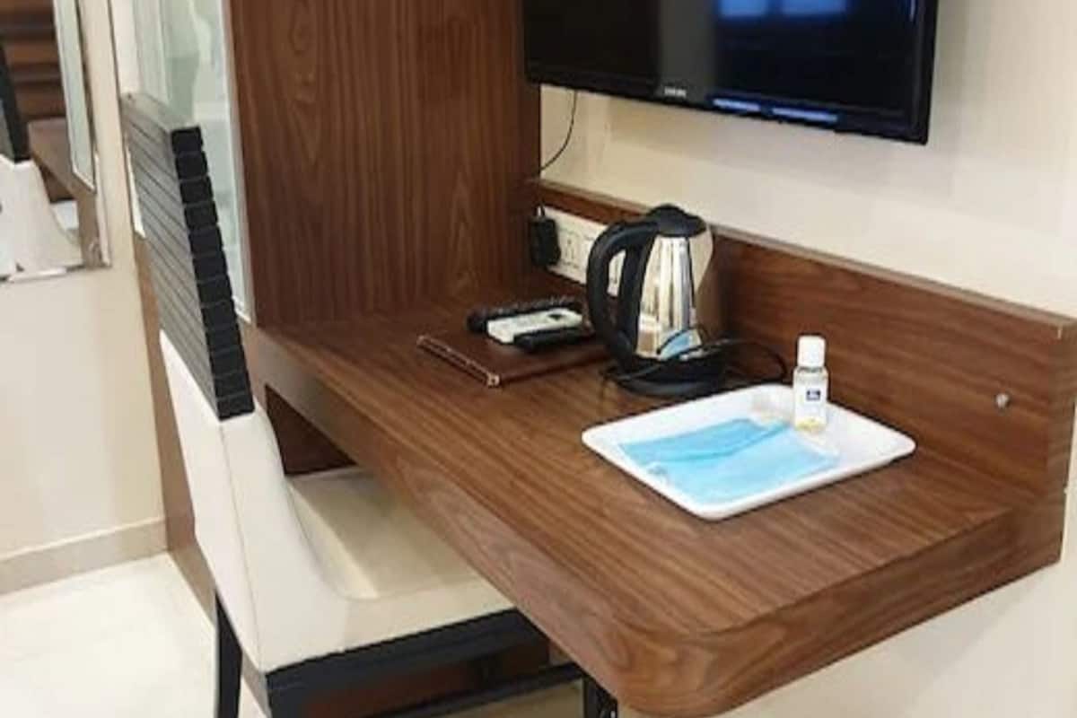A wooden desk with a flat-screen TV, a kettle, a cup, and a small plate.