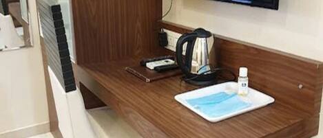Un escritorio de madera con un televisor de pantalla plana, una tetera, una taza y un plato pequeño.