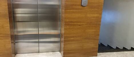 An elevator with a digital display, a wooden panel, and a marble floor with a circular design.