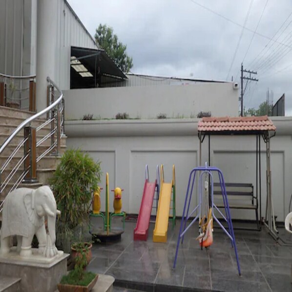 A rooftop playground with slides and swings, a staircase, and a statue of an elephant.