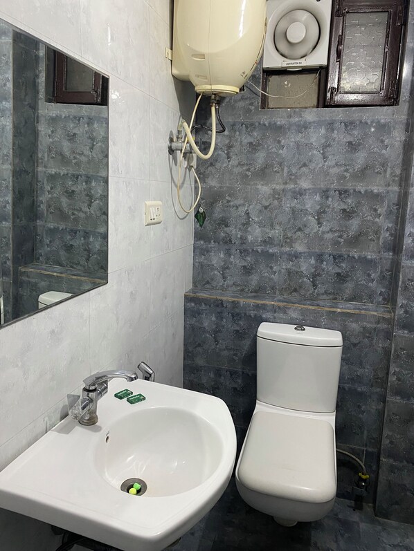 Une salle de bain avec un lavabo blanc, des toilettes, un miroir et un système de ventilation fixé au mur.