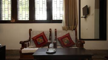 A room with a wooden sofa, a small table with a glass object, and a TV mounted on the wall.