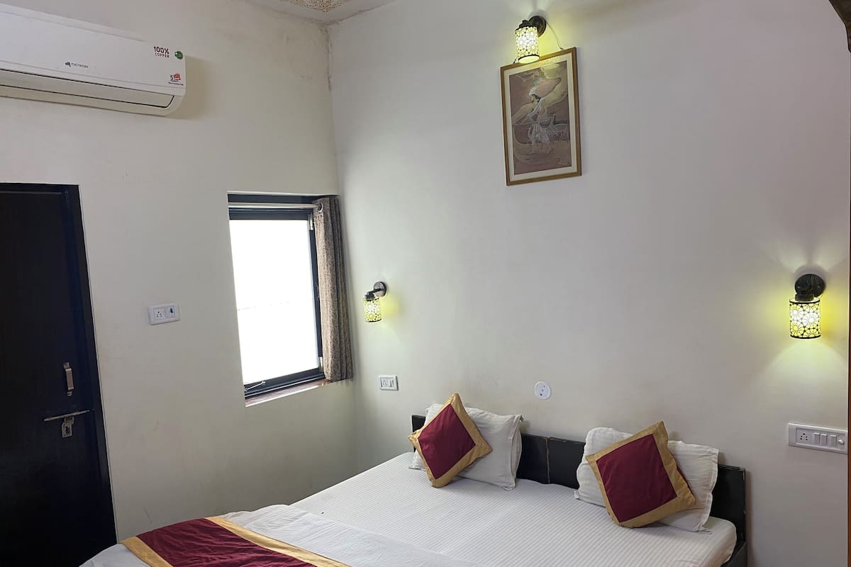 Habitación de hotel con cama, ventana, luces fijadas a la pared y un equipo de aire acondicionado.