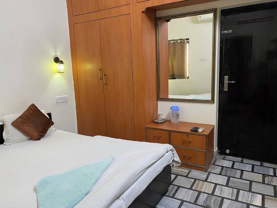 Habitación de hotel con cama, armario, mesita de noche con lámpara, espejo y puerta.