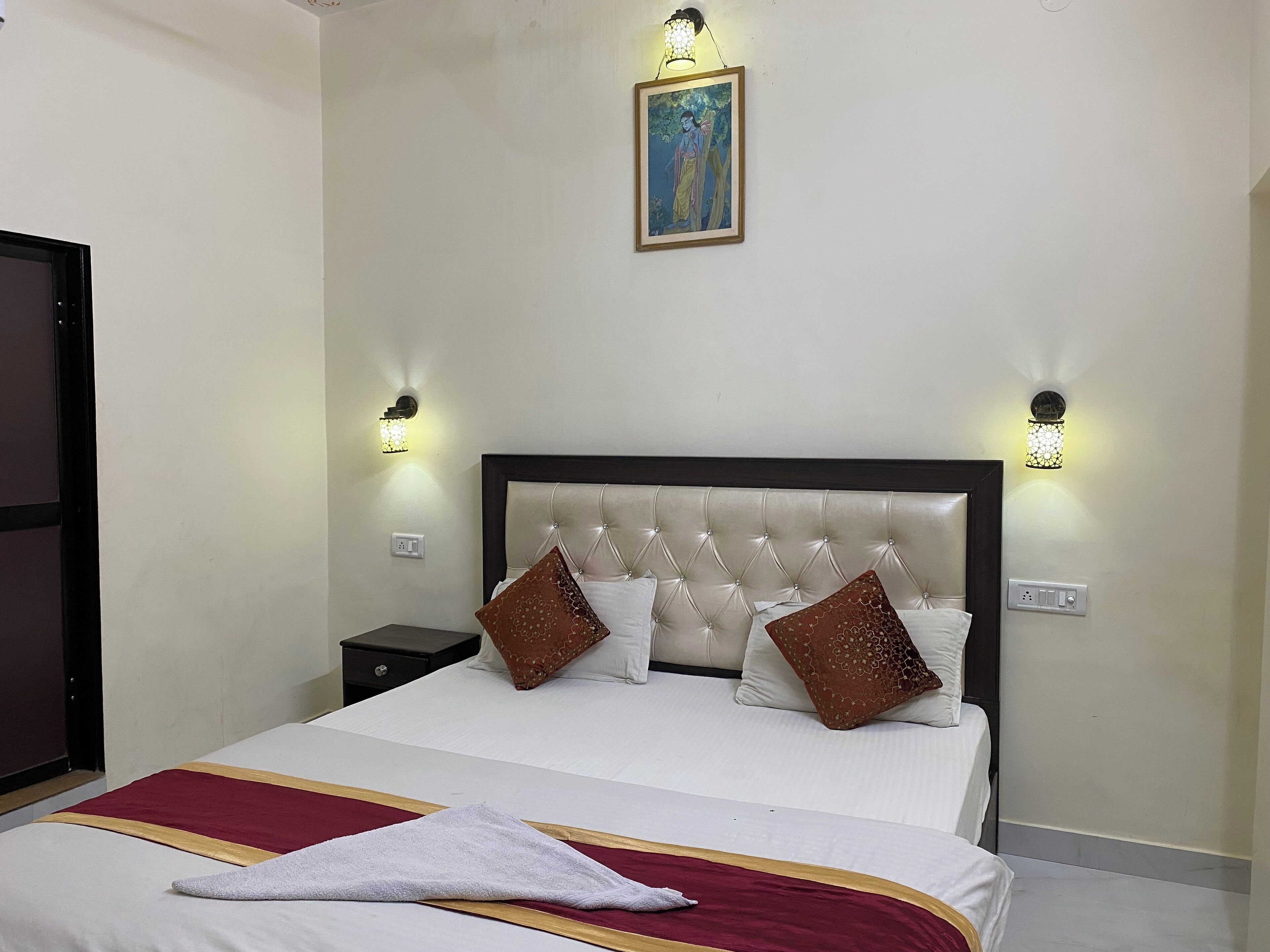 A hotel room with a large bed, two nightstands, wall sconces, a framed picture, and a red and white striped bed runner.