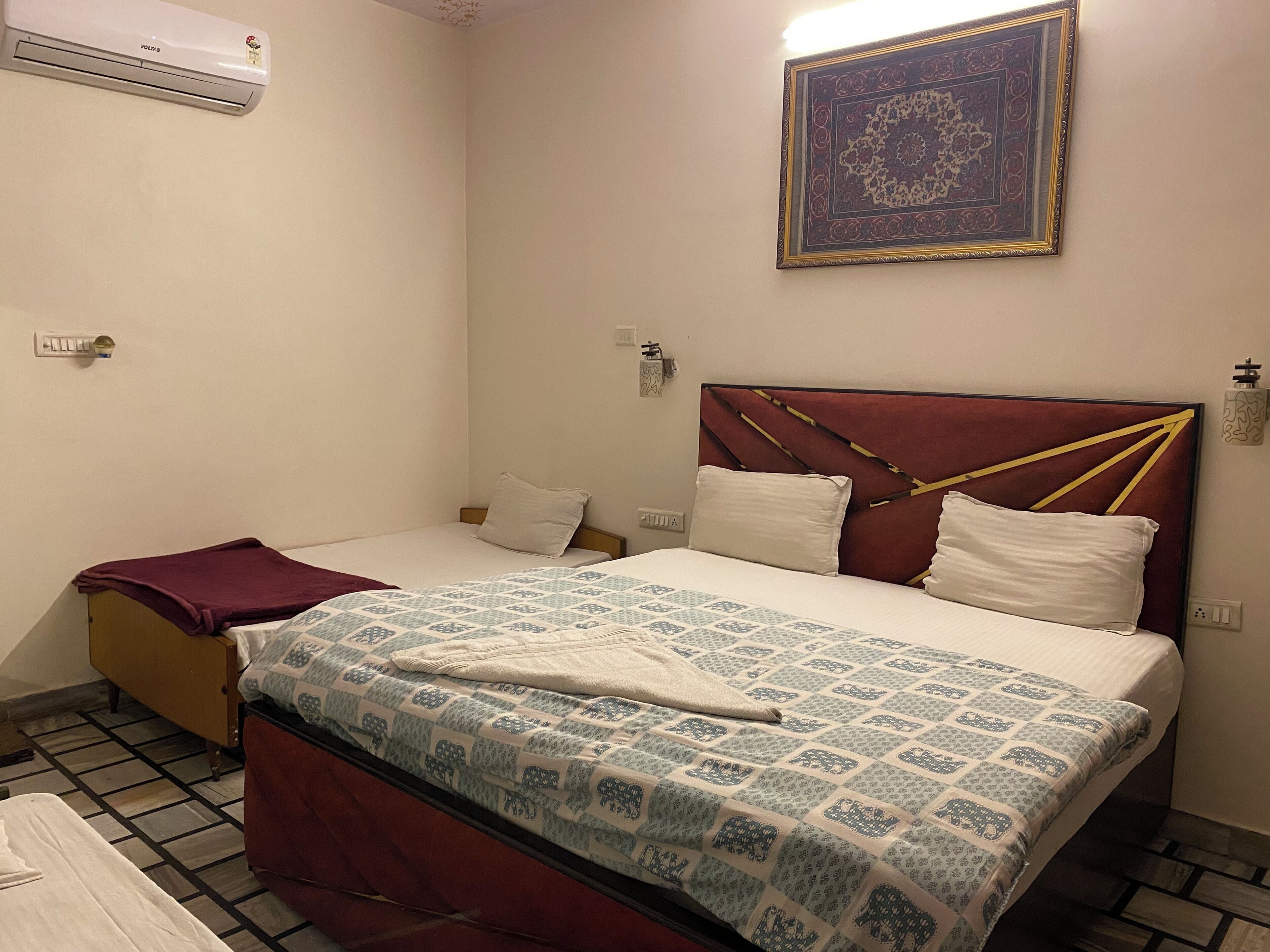 Un dormitorio con cama, mesita de noche, aire acondicionado montado en la pared y un adorno en la pared.