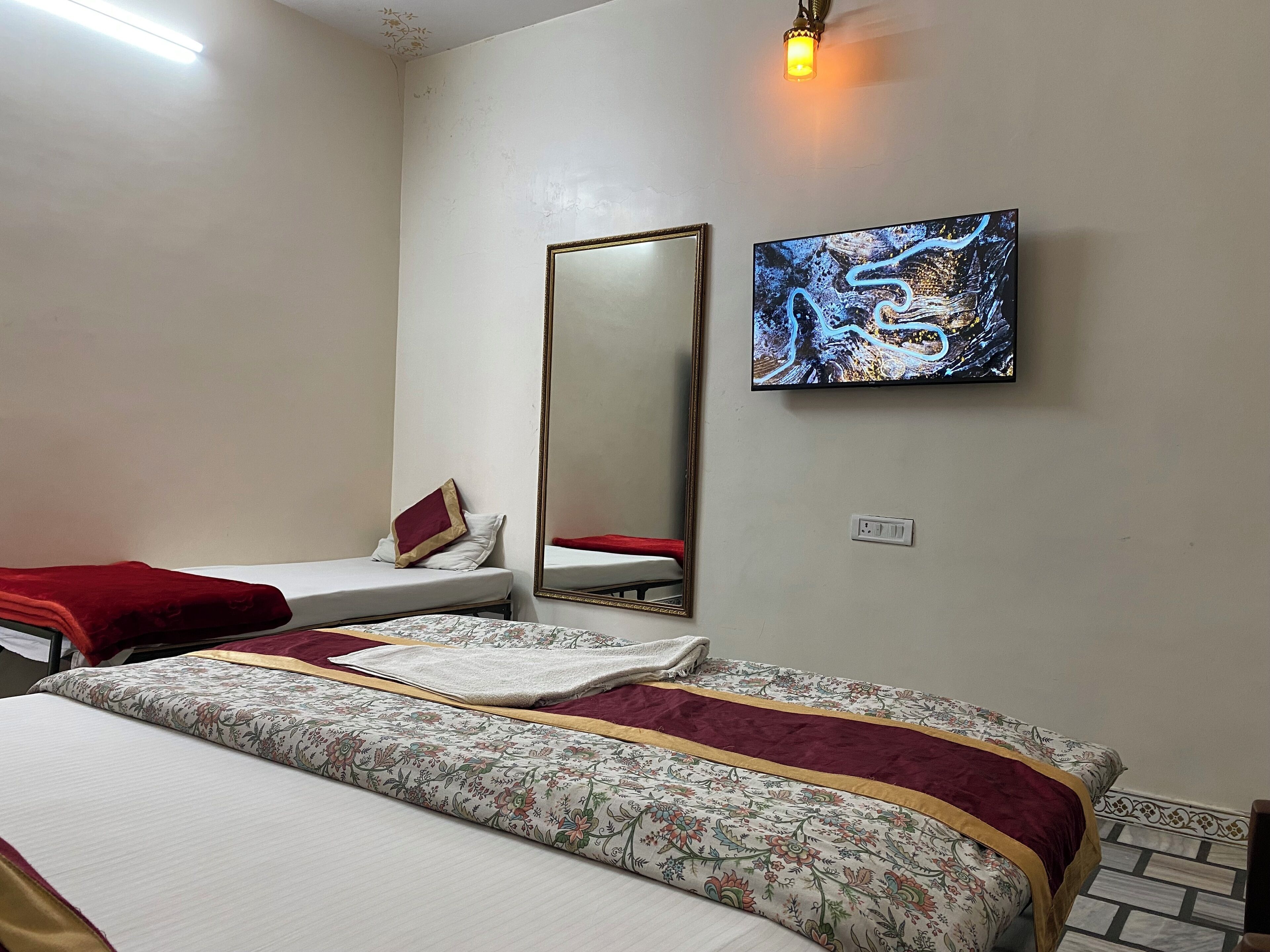 Habitación de hotel con dos camas, un espejo grande, un televisor montado en la pared y una lámpara pequeña.
