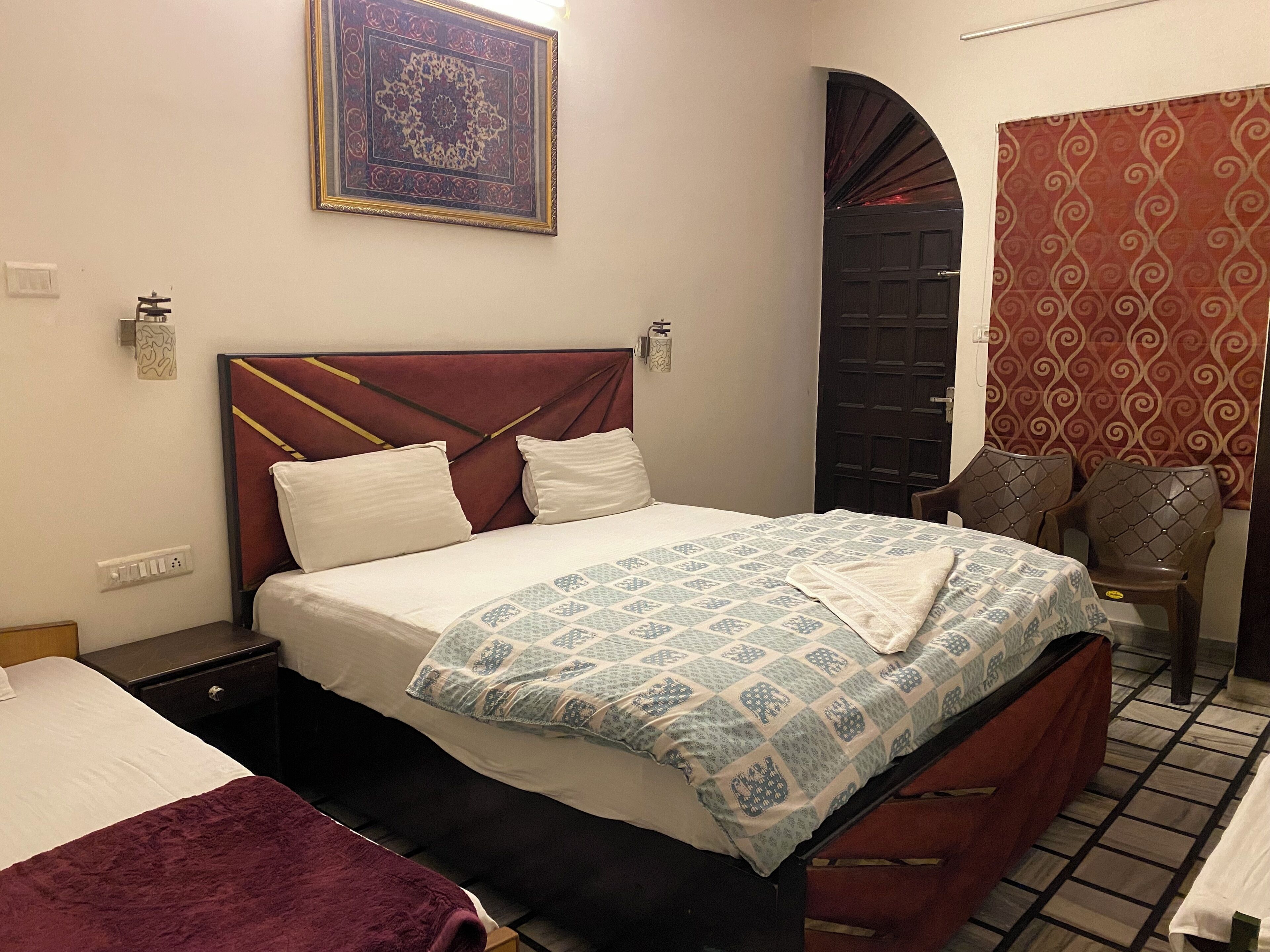 Une chambre d’hôtel avec un lit, une table de chevet, une chaise, une porte et un rideau à motifs.