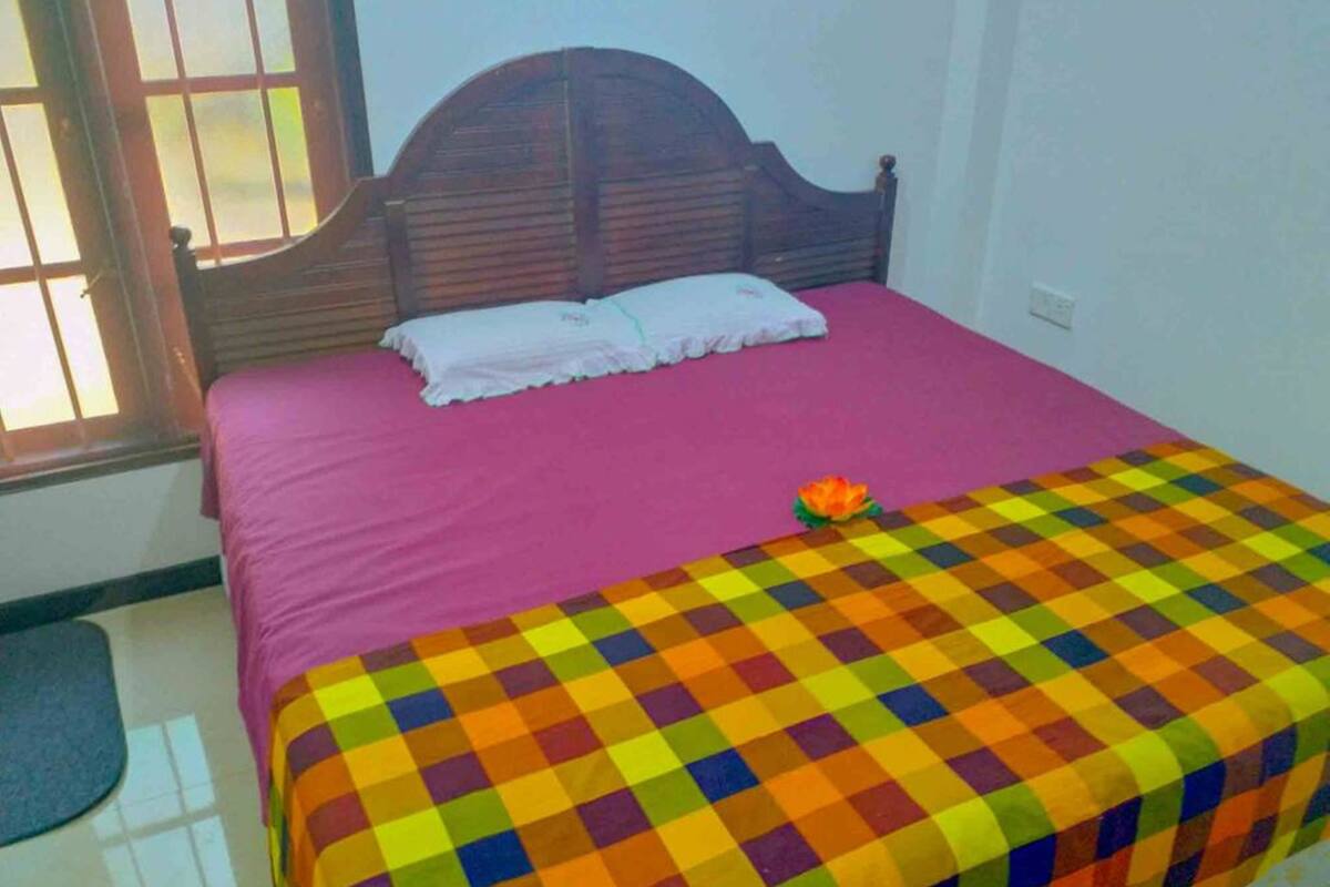 Una cama con cabecera de madera, una colcha rosa y una manta multicolora a cuadros.