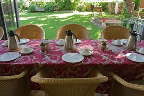 A table set for four with a red tablecloth, wicker chairs, and a view of a garden. - Alte Remise (Dresden)