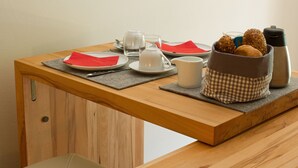 A wooden table with a breakfast setup including plates, cups, a pitcher, and a basket of bread. - Alte Remise (Dresden)