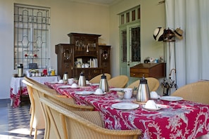 A dining area with tables set for a meal, wicker chairs, a cabinet with glassware, and a lamp. - Alte Remise (Dresden)