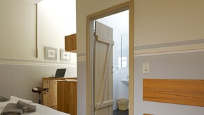 A bedroom with a bed, a desk with a laptop, a wooden headboard, and a bathroom visible through an open door. - Alte Remise (Dresden)
